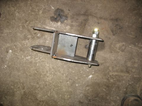 1995 Ford C-350 (Centurion Conversions) - A fabricated metal part, likely for a vehicle's suspension system, rests on a rough concrete surface.