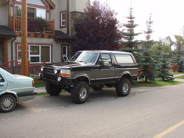 Lifted black Ford Bronco 3/4 front view on mud tires with chrome wheels and four driving lights