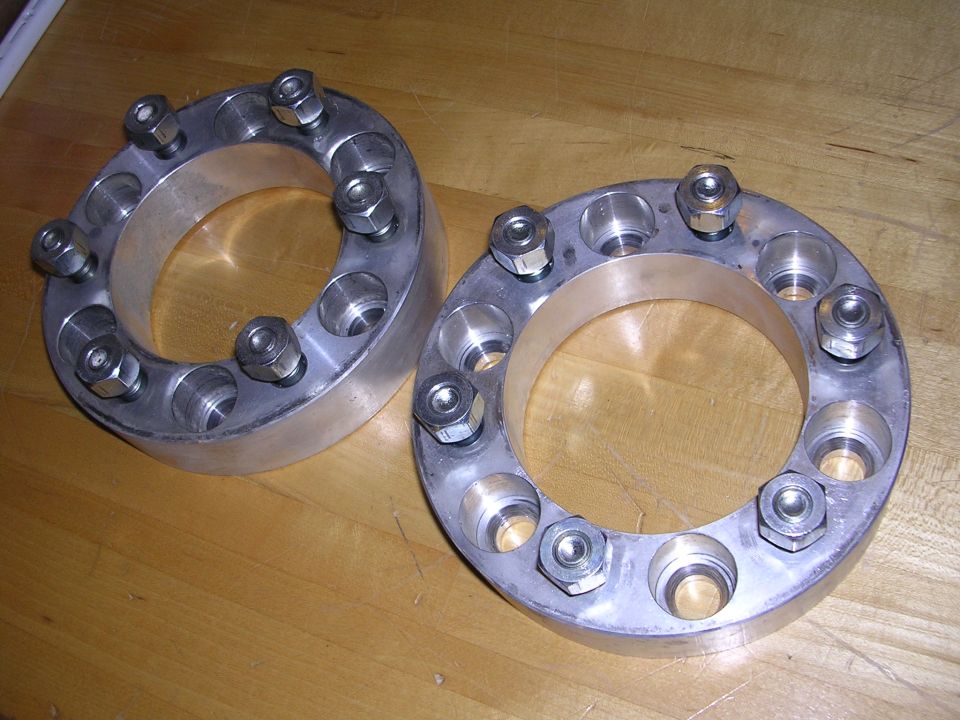 Two silver wheel spacers with lug nuts on a wooden surface.