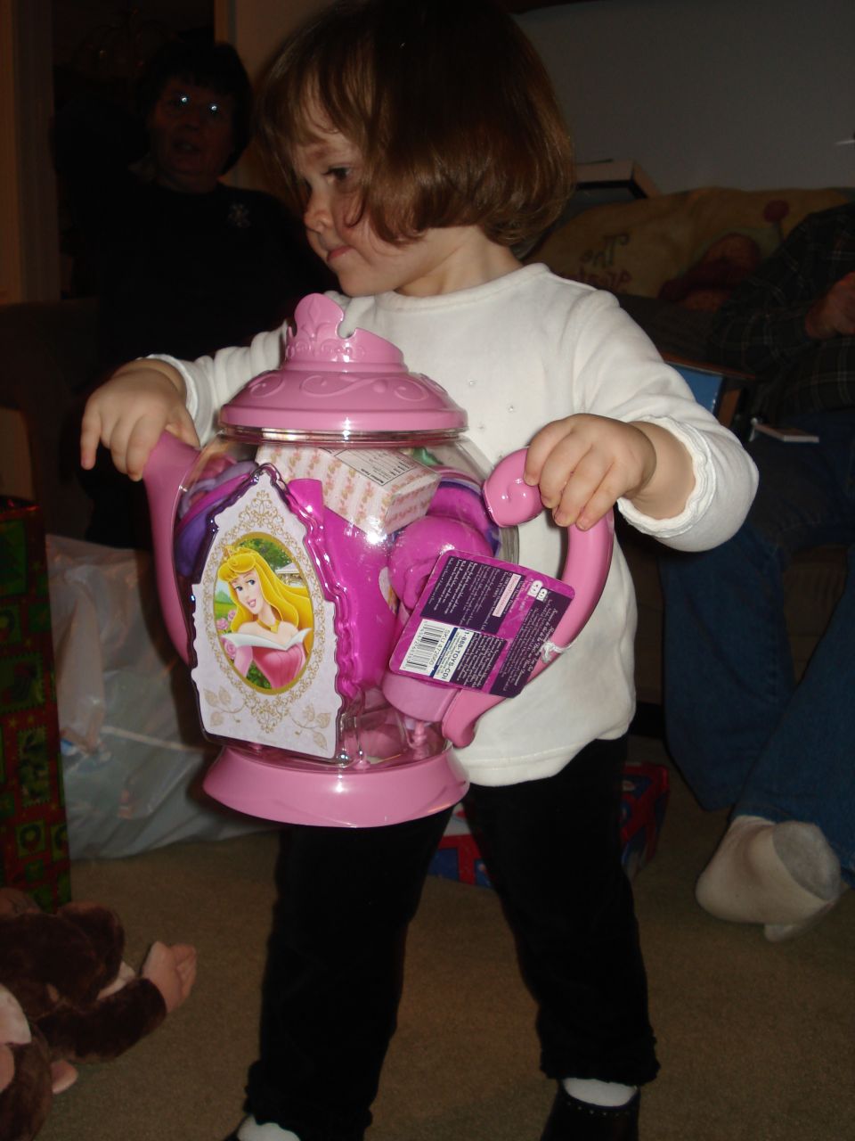 Young child holding a pink toy teapot with Princess Aurora on it.