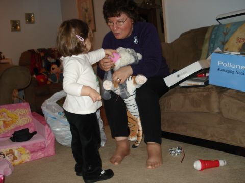 2000 Ford Crown Victoria - A woman sits on a couch holding a stuffed tiger while a young child stands in front of her, reaching out to the toy. A pink child's chair w…