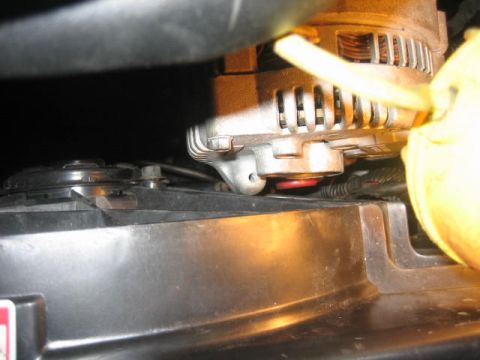 1996 Ford Thunderbird - A close-up view shows the alternator mounted above a black fan shroud. The alternator has a silver casing with cooling fins and a yellow wi…