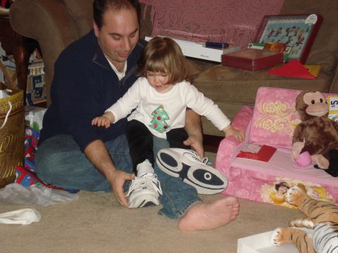 2000 Ford Crown Victoria - A father is helping his young daughter put on her shoes while sitting on the floor. They are surrounded by gifts and toys, suggesting a hol…