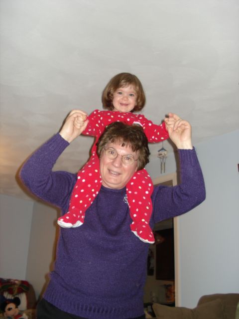 2000 Ford Crown Victoria - A woman carries a young child on her shoulders. The child is wearing a red and white polka dot outfit, and the woman is wearing a purple sw…