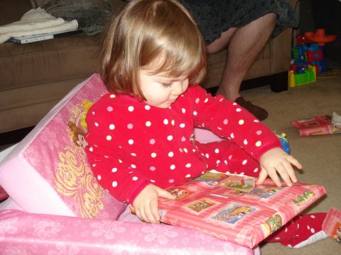 2000 Ford Crown Victoria - A young child in a red and white polka dot pajama set is sitting on a pink chair and opening a gift wrapped in pink paper with cartoon char…