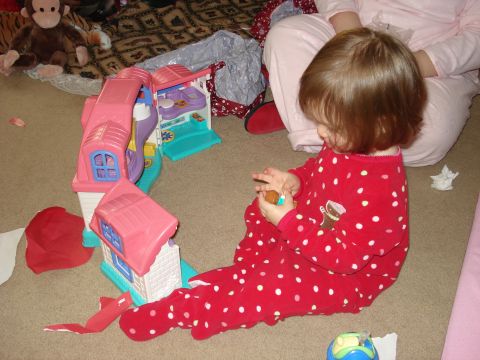 2000 Ford Crown Victoria - A young child in a red polka dot pajama set is playing with a pink toy house on the floor. A stuffed monkey is visible in the background.