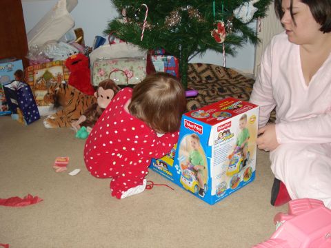 2000 Ford Crown Victoria - A young child in red polka dot pajamas is playing with a Fisher-Price Little People toy box next to a Christmas tree. A woman in a pink rob…