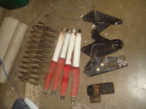 1992 Ford Bronco - Suspension lift components laid out on a concrete garage floor: two tan coil springs, four white Rancho shocks with red bellows boots, a br…