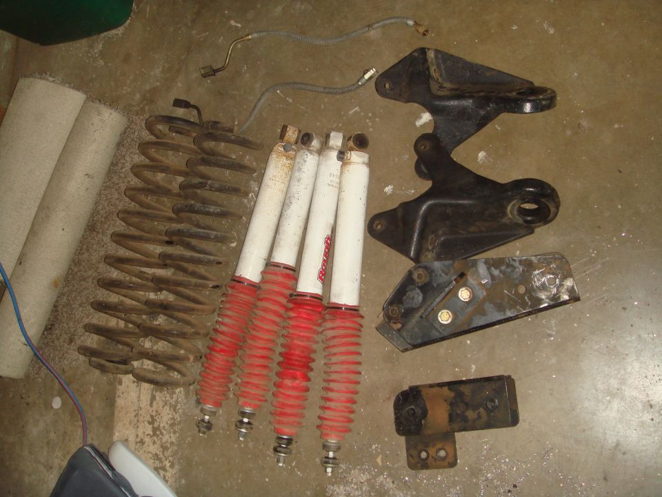 Lift kit parts on garage floor: coil springs, white Rancho shocks with red boots, steel brackets