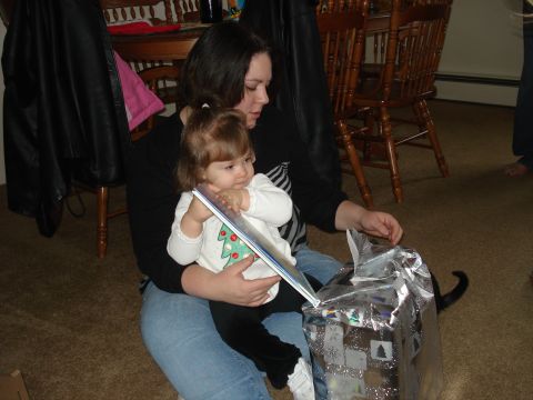 2000 Ford Crown Victoria - A woman is holding a baby on her lap and they are looking at a book. A wrapped gift is in front of them.