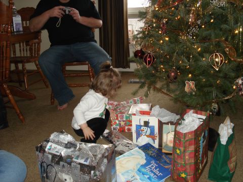 2000 Ford Crown Victoria - A young child is crouching on the floor near a Christmas tree and presents. A person is sitting in a chair in the background, holding a cam…