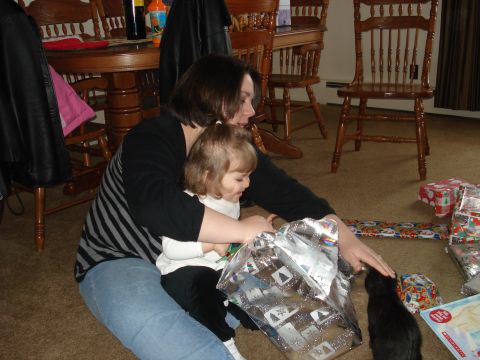 2000 Ford Crown Victoria - A woman and a young child are sitting on the floor, opening presents. A black kitten is looking at the presents.