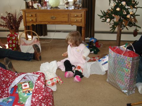2000 Ford Crown Victoria - A young child in a pink outfit sits on the floor surrounded by Christmas gifts and decorations. A Christmas tree with lights and ornaments…