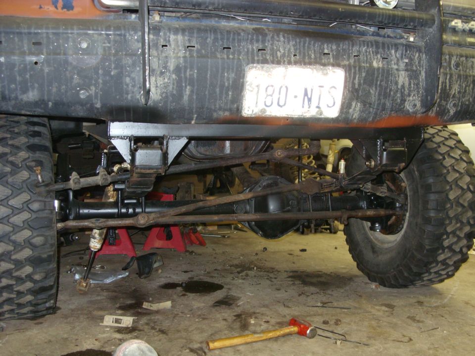 Rear leaf springs and suspension components on a lifted truck with a license plate reading 180-NIS