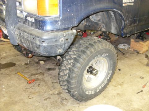 1988 Ford Bronco - The front end of a blue Ford truck is shown with a large tire and bumper, indicating it is undergoing maintenance or modification.