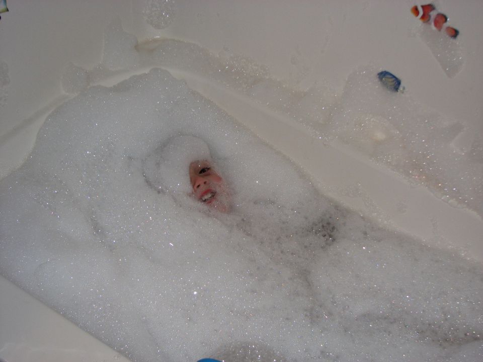 Child submerged in bathtub bubbles with clownfish toy