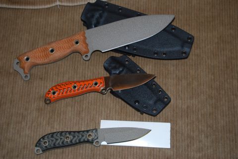 1991 Ford Bronco - A collection of three knives, each with a different handle design and a black sheath, are displayed on a textured brown background.
