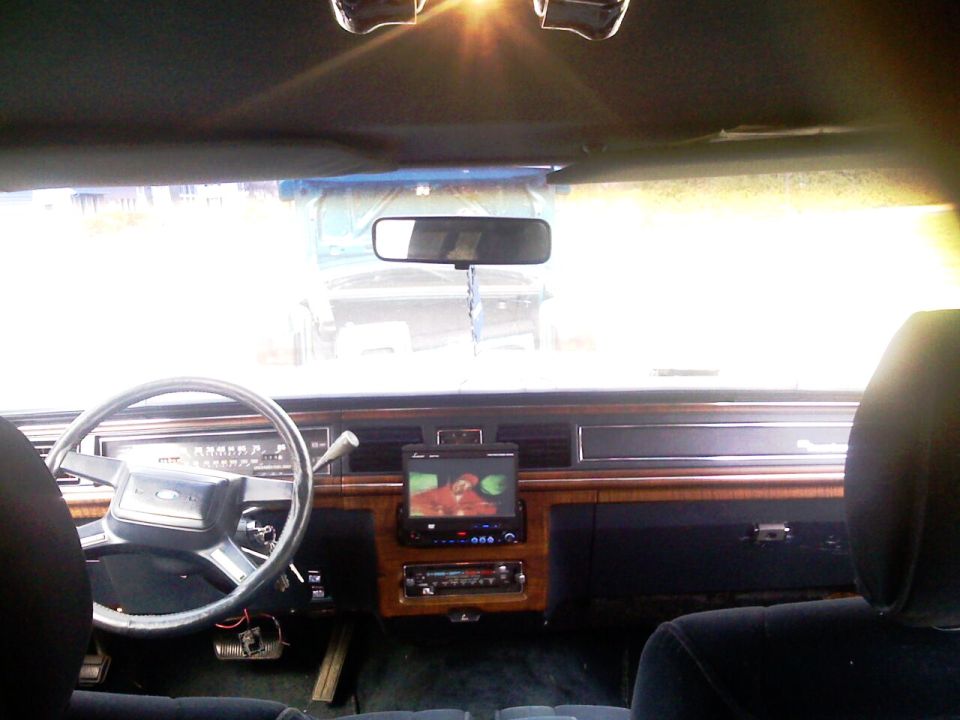 Crown Victoria interior with woodgrain dash, Ford steering wheel, and aftermarket flip-out screen stereo playing video.