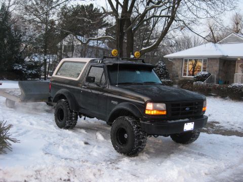 1995 Ford Bronco - Black 1995 Ford Bronco with a light bar and smiley face lights on the roof is parked in the snow, towing a trailer.