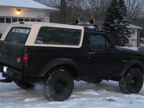 1995 Ford Bronco - A black Ford Bronco with a tan removable top is seen from the side in a snowy environment, with smoke coming from the exhaust.