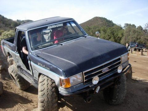 1989 Ford Bronco - Modified Ford Bronco with large tires navigating rough terrain, another truck visible in background.