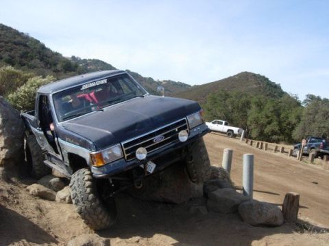 1989 Ford Bronco - A dark blue Ford Bronco navigates a rocky trail, demonstrating its off-road capabilities.