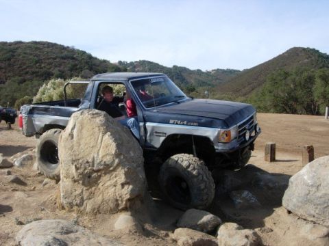1989 Ford Bronco - This modified truck is tackling a challenging off-road course with large rocks.