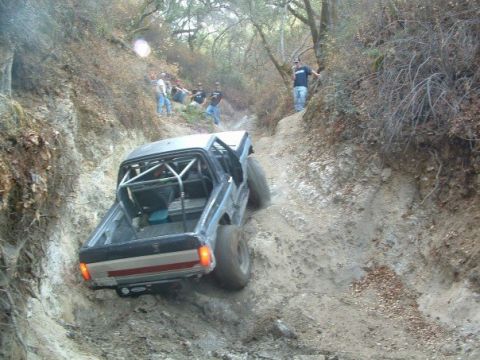 1989 Ford Bronco - A modified off-road truck navigates a challenging dirt path with spectators watching.