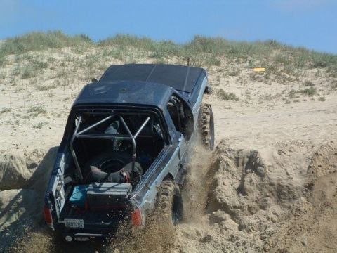 1989 Ford Bronco - This modified SUV is navigating a challenging sandy terrain, with its rear end angled upwards.