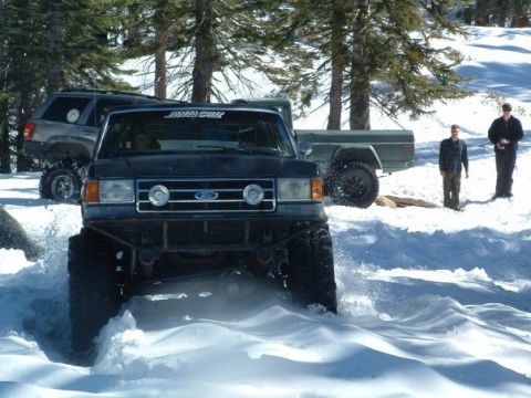 1989 Ford Bronco - Multiple vehicles navigate a snowy terrain with trees in the background.