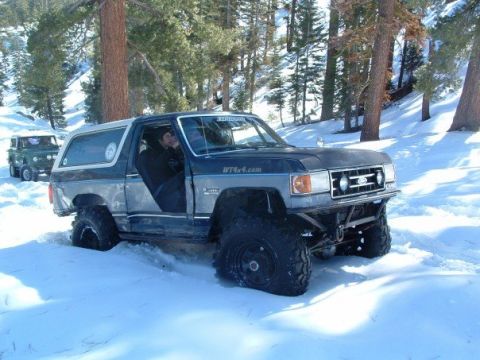 1989 Ford Bronco - A modified Ford Bronco navigates a snowy terrain, with a Jeep visible in the distance.