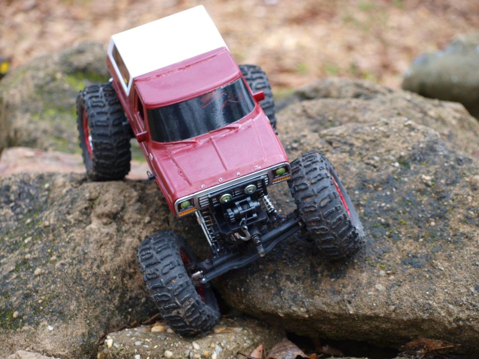 Red and white RC Ford rock crawler climbing rocks, front 3/4 view