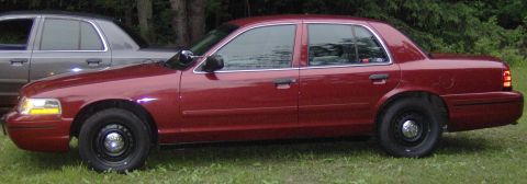 2000 Ford Crown Victoria - A red Ford Crown Victoria is parked on grass, with another car visible behind it.
