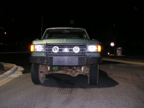 1989 Ford Bronco - This green Ford truck is shown at night with its headlights and auxiliary lights on.