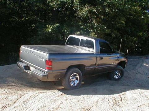 1989 Ford Bronco - This Dodge Ram pickup truck features a bed cover and is parked on a dirt surface with tire tracks visible.