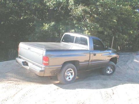 1989 Ford Bronco - A gray Dodge pickup truck is parked on a dirt surface with trees in the background.