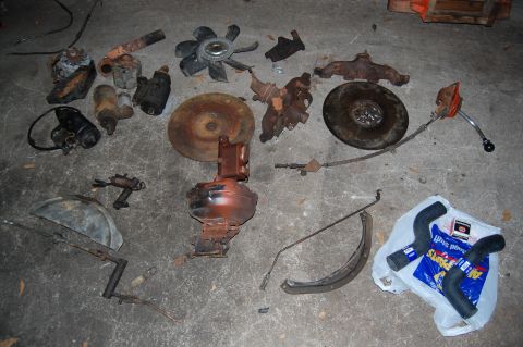 1994 Ford Bronco - A collection of old vehicle parts, including engine components and hoses, are scattered on a garage floor.