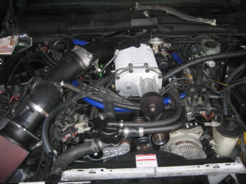 1996 Ford Thunderbird - A detailed view of a supercharged engine bay, likely from a 1996 Ford Thunderbird, showcasing a prominent silver supercharger, black intake…