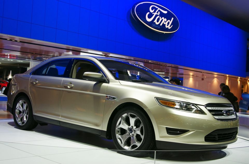 Tan Ford Taurus sedan on display with Ford logo in background