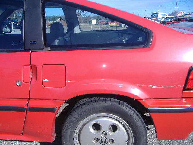 Red coupe rear passenger side, showing fuel door and dented quarter panel.