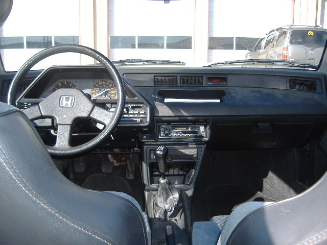 Interior view of a car dashboard with steering wheel, gauges, radio, and gear shifter.