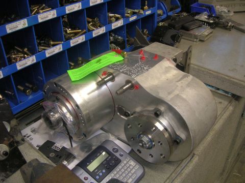 1996 Ford Bronco - A large metal gearbox is shown in a workshop setting, with shelves of hardware in the background and a label maker and other electronic dev…
