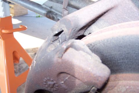 1990 Ford Bronco - A close-up view of a rusty brake caliper and rotor assembly, likely from a 1990 Ford Bronco, supported by an orange jack stand.