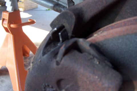 1990 Ford Bronco - A close-up view of a rusty brake caliper and rotor assembly, supported by an orange jack stand.