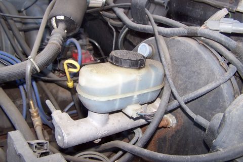 1990 Ford Bronco - Close-up view of the brake master cylinder and fluid reservoir within a vehicle's engine bay.