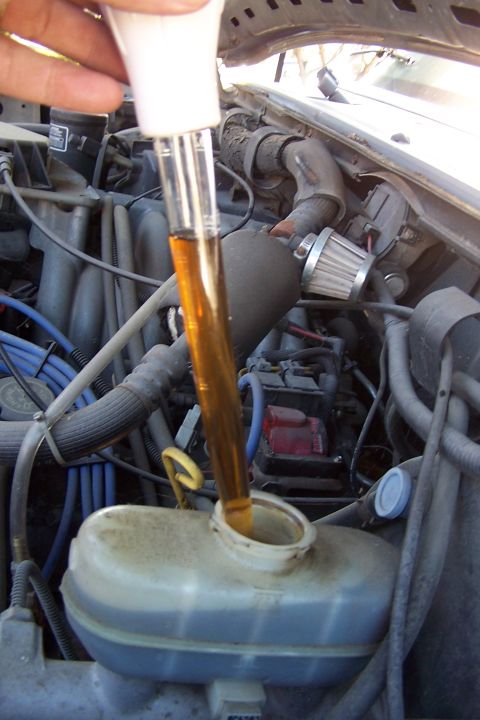 1990 Ford Bronco - Amber fluid is poured into a vehicle's reservoir from a glass tube in the engine bay.