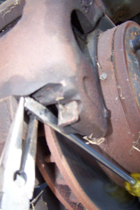 1990 Ford Bronco - A close-up view of a vehicle's brake rotor and caliper assembly, with tools being used for maintenance.