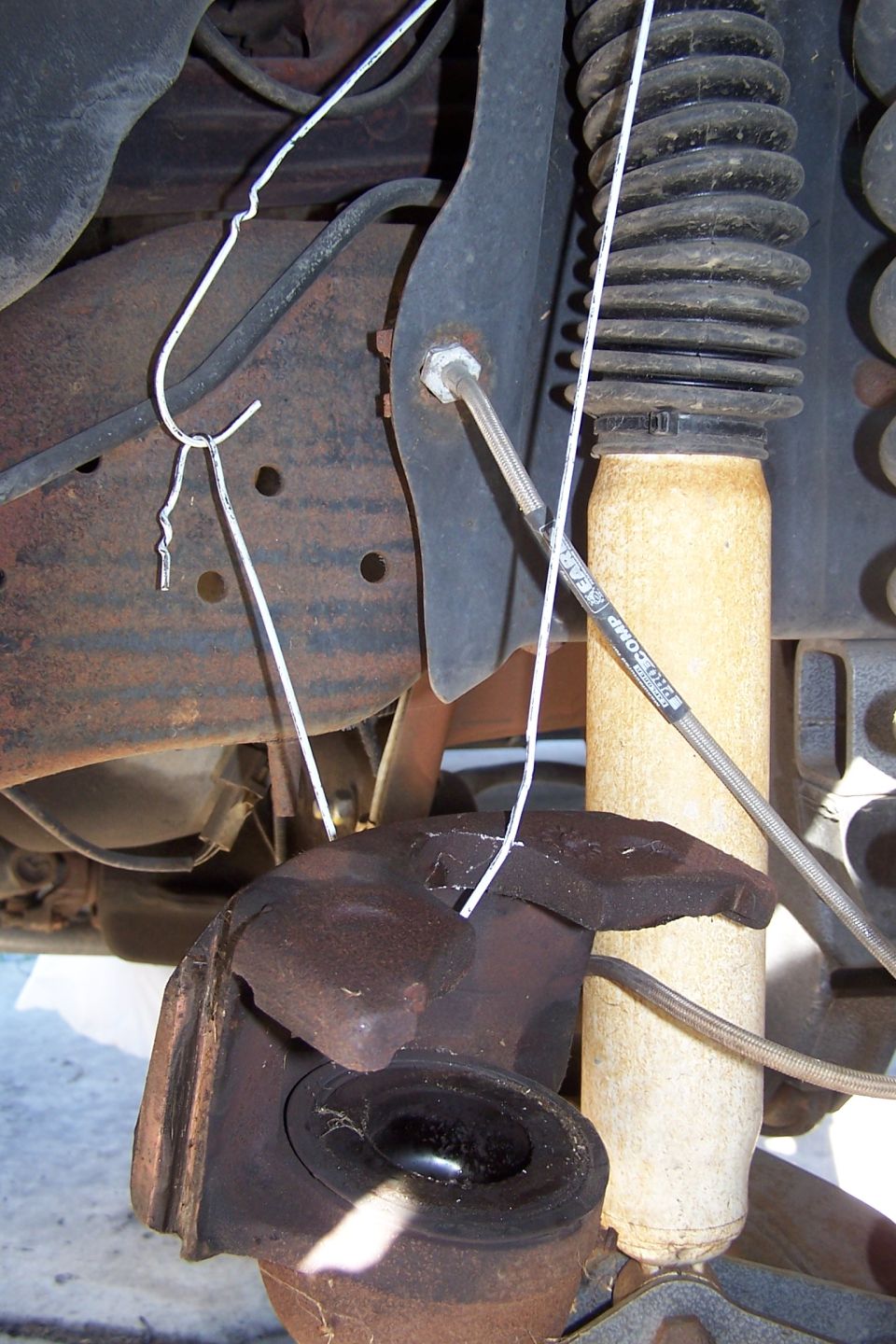 Rusty suspension part with a broken ball joint and white wire. Shock absorber visible