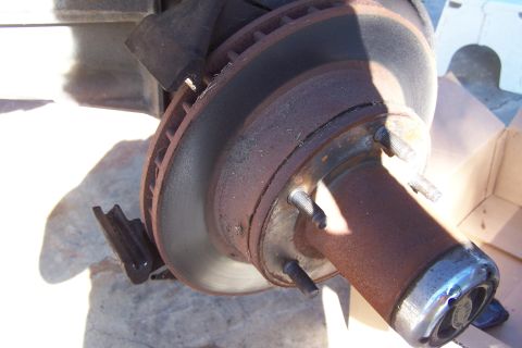 1990 Ford Bronco - Close-up view of a heavily rusted brake rotor and hub assembly, showing the studs and part of the suspension components.