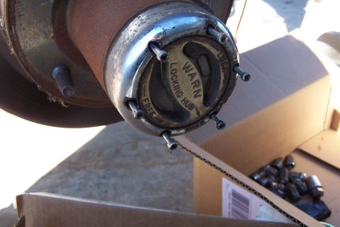 1990 Ford Bronco - A Warn locking hub is shown attached to a vehicle's wheel hub, with a box of lug nuts nearby.